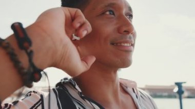 Close up, young man tourist sits on bench on the pier talking using headset