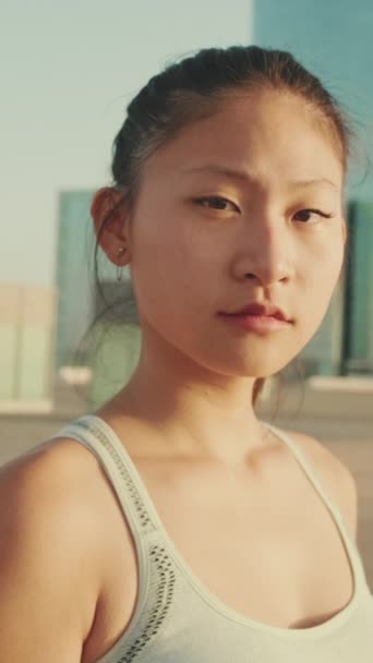 垂直方向のビデオ スポーツのトップスタンドのアジアの女の子は 近代的な建物の背景には カメラに見えます 前方に動くカメラ — ストック動画