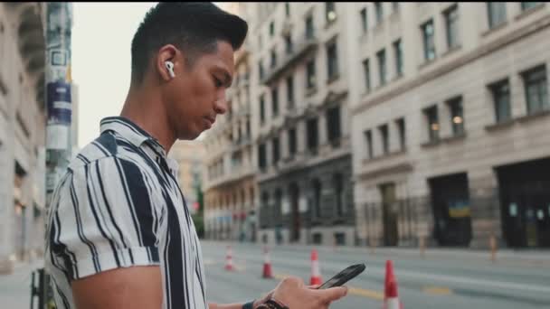 Anak Muda Mendengarkan Musik Dan Menggunakan Ponsel Saat Berdiri Penyeberangan — Stok Video