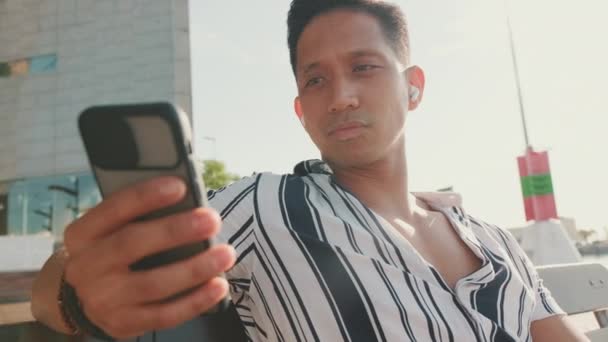 Junger Mann Sitzt Auf Bank Auf Seebrücke Und Benutzt Handy — Stockvideo