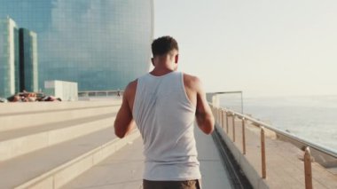 Young bearded male athlete doing workout, stretching on the embankment