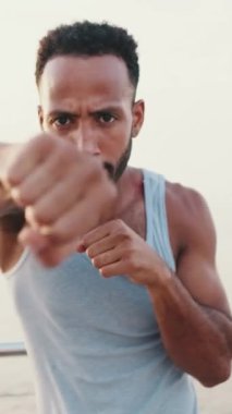 VERTICAL VIDEO: Close up, young bearded male fit athlete boxer practicing punching technique while standing on the embankment
