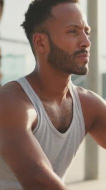 VERTICAL VIDEO: Young bearded male athlete is resting after training sitting on bench