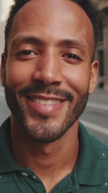 VERTICAL VIDEO: Close-up of happy young man standing on the street. Guy smiles at the camera