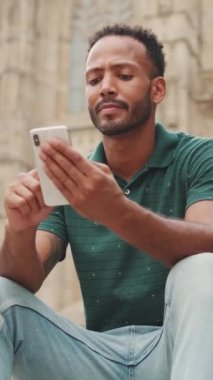 Genç adam Barcelona 'daki Sagrada Familia' nın merdivenlerinde otururken cep telefonu kullanıyor.