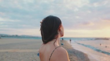 Sahilde durup güneşin doğuşunu izleyen genç bir kadın. Arka plan