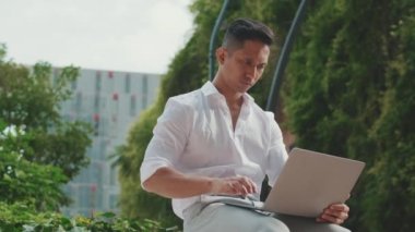 Genç işadamı iş merkezinin yanında otururken dizüstü bilgisayar kullanıyor