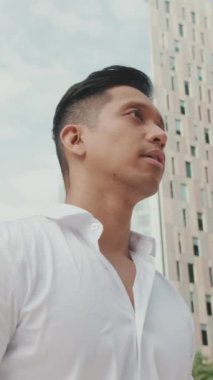 VERTICAL VIDEO: Close-up of young businessman standing on modern buildings background