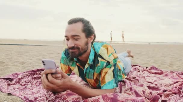 Uomo Sorridente Che Rilassa Sulla Spiaggia Con Smartphone Mano — Video Stock