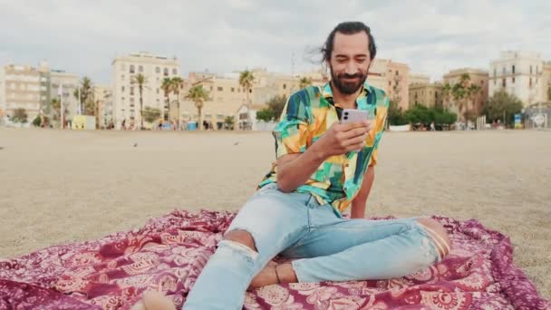 Νεαρός Χαρούμενος Άντρας Που Χρησιμοποιεί Κινητό Τηλέφωνο Στην Παραλία — Αρχείο Βίντεο
