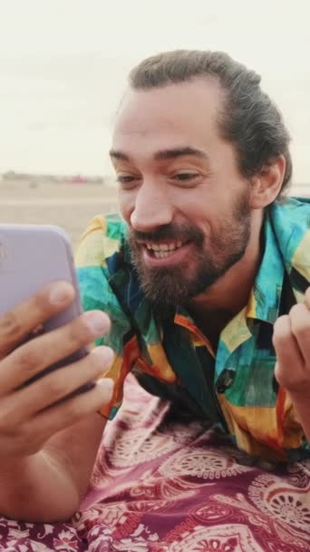 垂直ビデオ ビーチで携帯電話のビデオリンクで話している若い幸せな男 — ストック動画