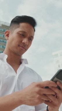 Genç işadamı iş yerinde dururken akıllı telefonuyla daktilo kullanıyor.