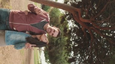 Gülen bir çift parkta dikilirken birbirlerine sarılıyor.