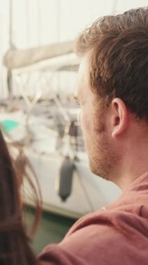 VERTICAL VIDEO: Close up, couple sitting in the port looking at the yachts