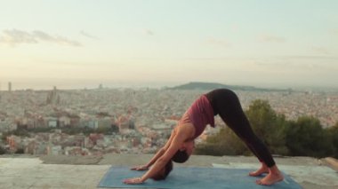 Genç bir kadın gün doğumunda izleme platformunda yoga yapıyor. Amanho mukha svanasana pozu