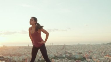 Young woman in bodysuit practices yoga at dawn at viewpoint. Girl raises her hands up