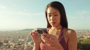 Kapalı, mutlu atletik kadın gözetleme noktasında dururken cep telefonu kullanıyor.