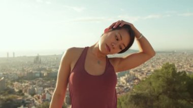 Young woman stretches her neck muscles while standing on an observation deck
