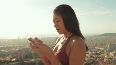 Kapalı, mutlu atletik kadın gözetleme noktasında dururken cep telefonu kullanıyor.