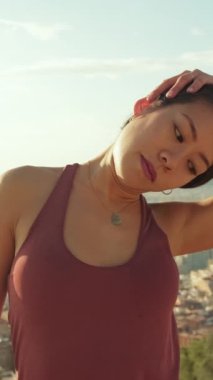 VERTICAL VIDEO: Young woman stretches her neck muscles while standing on an observation deck