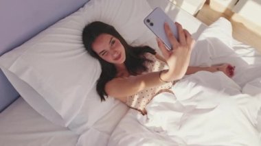 Yatakta yatan genç ve güzel bir kadının sabah selfie 'si. Üst görünüm