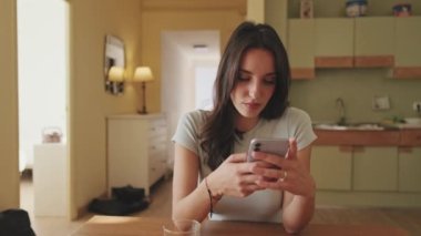 Young woman using smartphone while sitting in the kitchen