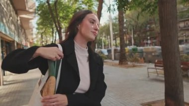 Güzel genç bir kadın alışveriş çantasıyla sokakta yürüyor.