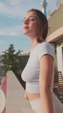 VERTICAL VIDEO, balkonda dururken güzel manzaranın tadını çıkaran genç bir kadın