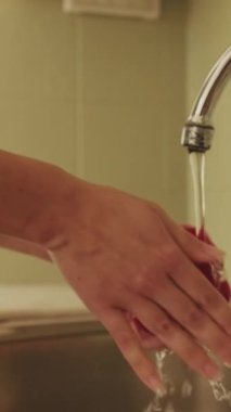 VERTICAL VIDEO, mutfakta dururken genç bir kadının ellerini yıkarken yakın plan.