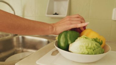 Ön plandaki kasede taze sebzeler, arka plandaki kız sebzeleri yıkar.