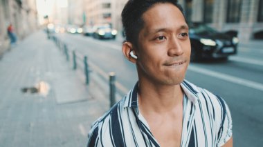 Genç adam yolun kenarında yürüyor ve kulaklıkla müzik dinliyor.