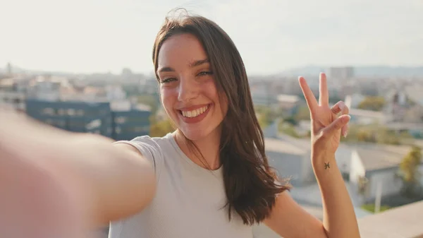 Genç bir kadının balkonda dururken selfie çekerken el sallaması işareti çekerken.