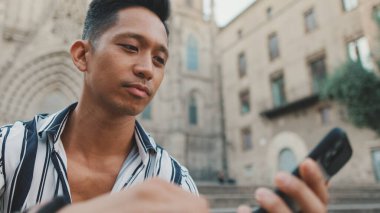 Basamaklardaki genç turist, arka planda otururken cep telefonu kullanıyor