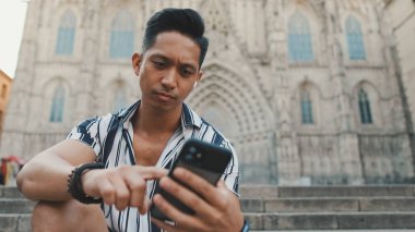 Basamaklardaki genç turist, arka planda otururken cep telefonu kullanıyor