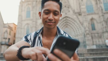 Basamaklardaki genç turist, arka planda otururken cep telefonu kullanıyor