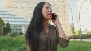 Modern binalarda otururken akıllı telefondan konuşan gülümseyen genç kız.