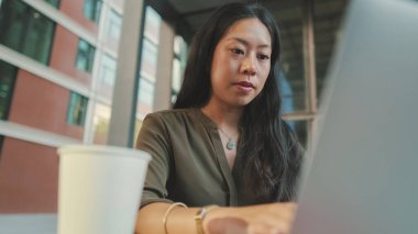 Dizüstü bilgisayarda çalışan ve kahve içen genç bir kadın.