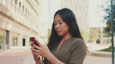 Modern binaların arka planında dururken cep telefonu kullanan genç mutlu iş kadınının yakın çekimi