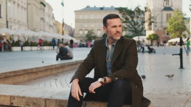 Sakallı adam eski kasabanın meydanında oturuyor.