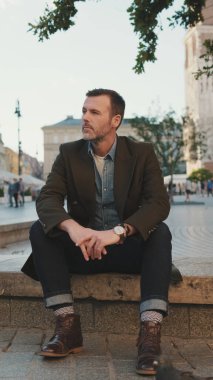 Sakallı adam eski kasabanın meydanında oturuyor.