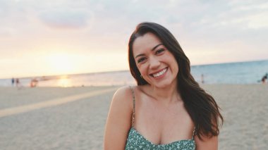 Genç kadın gözlerini açar ve kumsalda dururken kameraya gülümser.