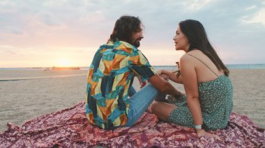 Erkek ve kadın gün doğumunda sahilde birbirleriyle konuşuyorlar.