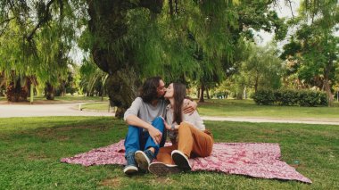 Mutlu, gülümseyen çift parkta battaniyede otururken konuşuyor.