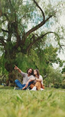 Mutlu, gülümseyen çift parkta battaniyede otururken konuşuyor.