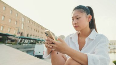 Deniz manzarasında cep telefonu kullanan gülümseyen genç bir kadın.