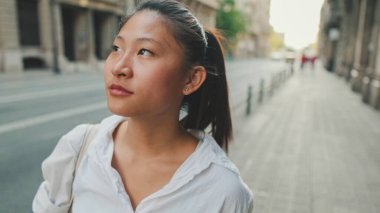 Genç bir kadın sokakta yürür ve etrafa bakar.