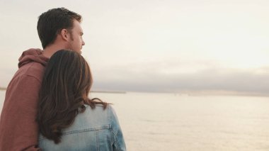 Deniz manzaralı arka planda birbirine sarılan genç bir çift. Arka plan