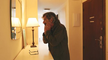 Yaşlı, yorgun, bavulla eve dönüyor ve aynada kendine bakıyor..