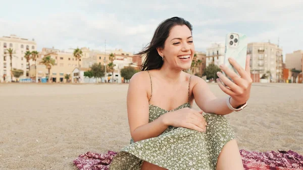 年轻女子坐在沙滩上 用手机 做录像机 — 图库照片