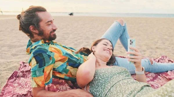 年轻夫妇在海滩上放松 一边聊天 一边用手机 — 图库照片